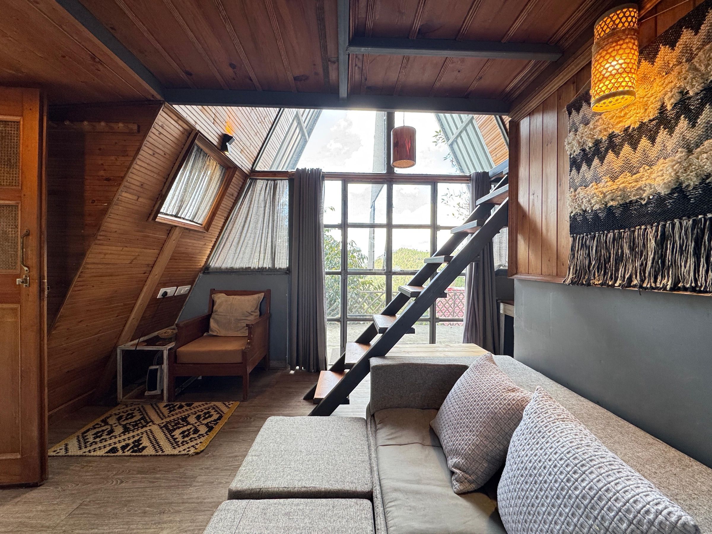 The A-frame sitting room, with a sofa, a woven wall hanging and a steep stair to the loft