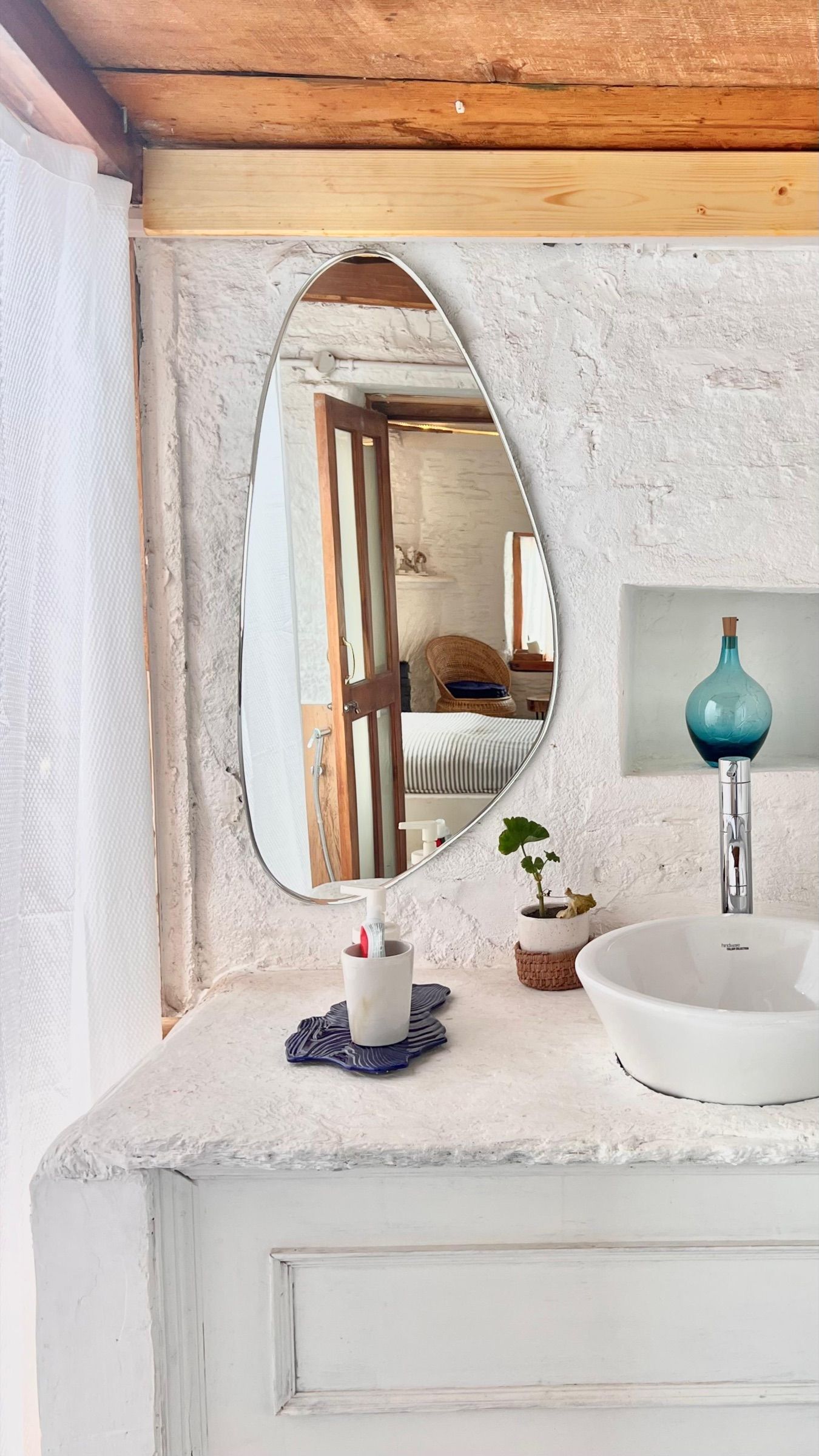 A blue glass bottle in a niche in a whitewashed wall, next to a pebble-shaped mirror
