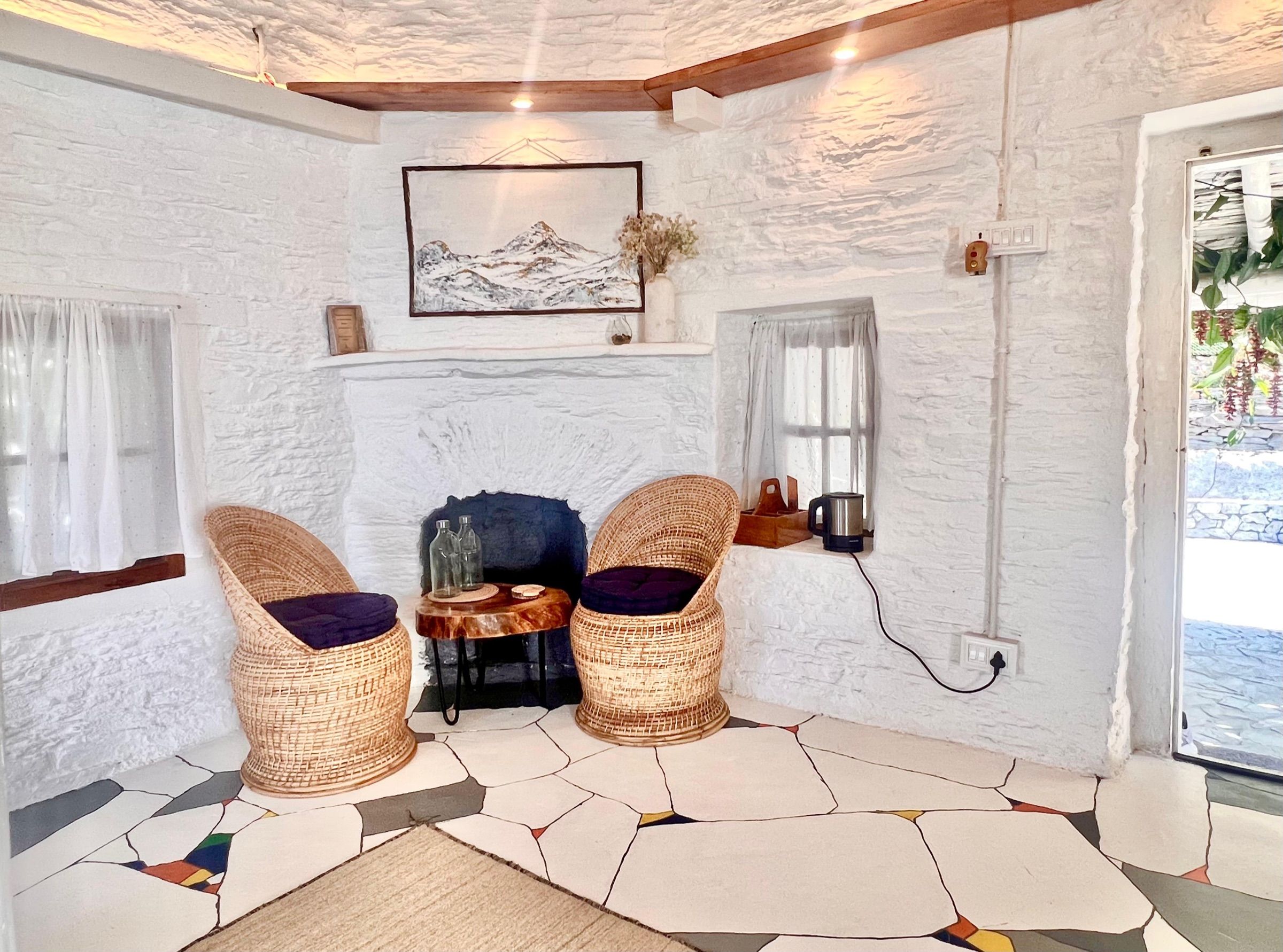 Two cane chairs by an old whitewashed fireplace in Kintsugi, with a painting of the mountains above