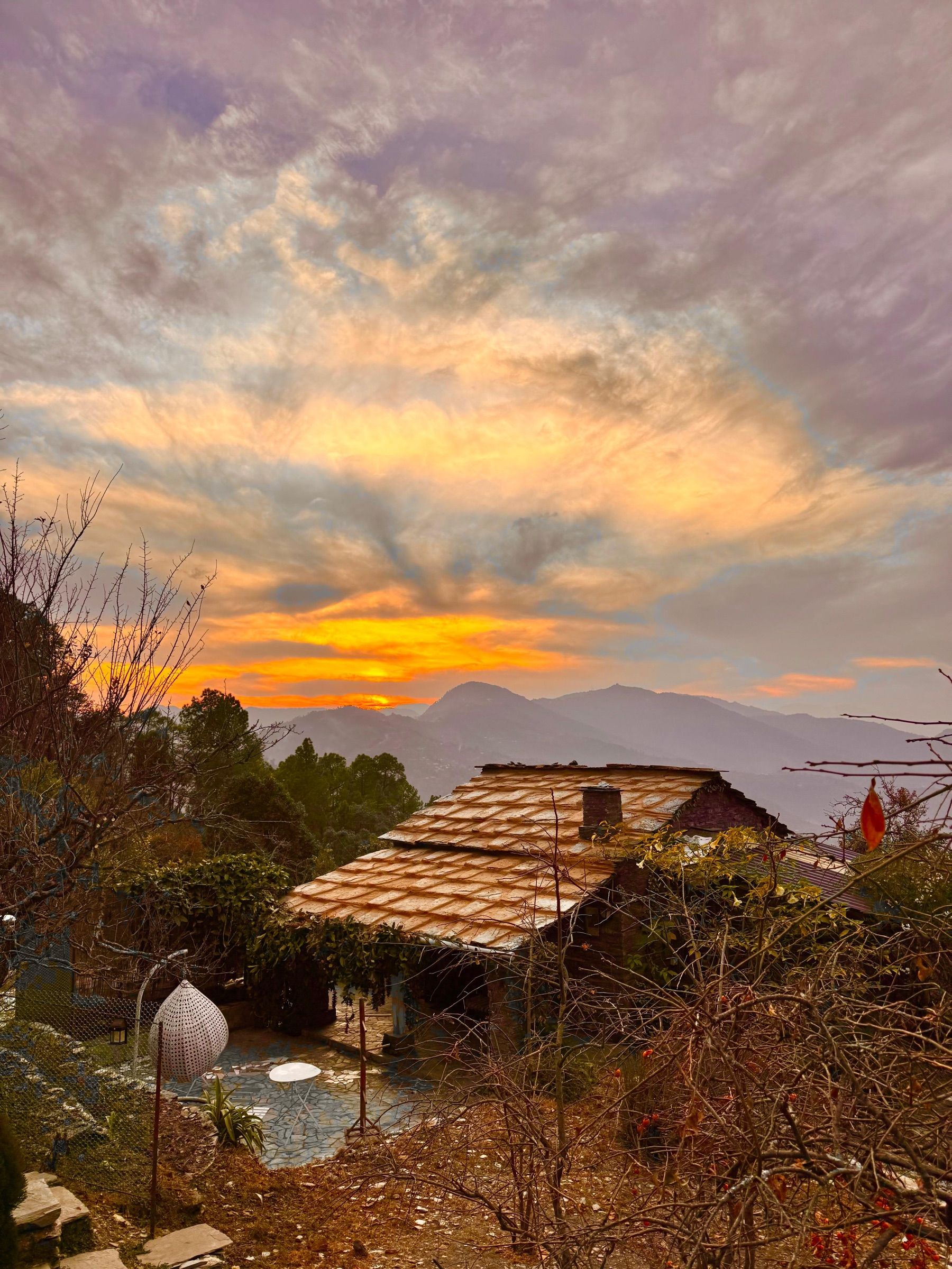 Sunset over the slate roof of a stone house, with the hills behind
