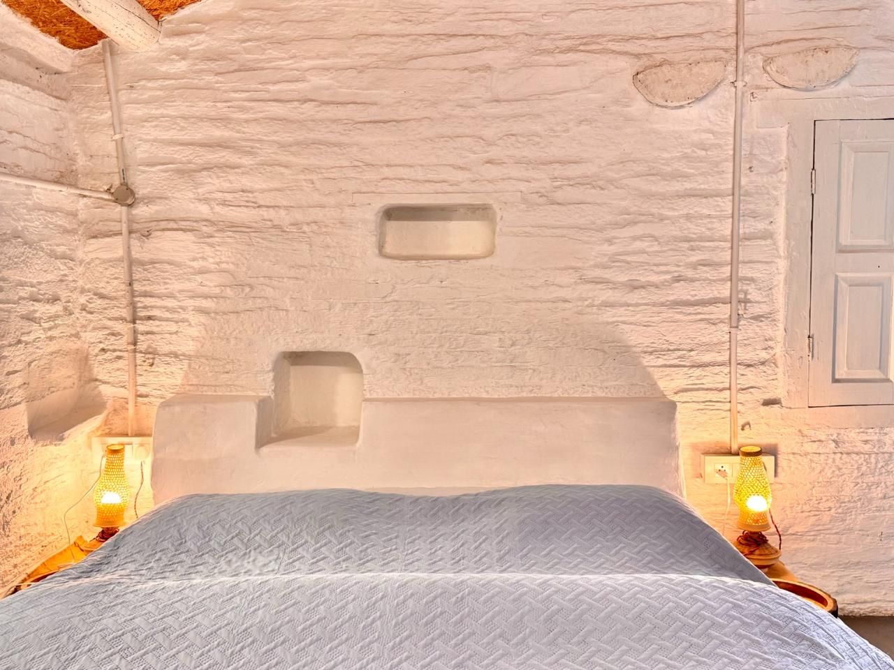 A whitewashed wall with small niches above the bed and two amber lamps