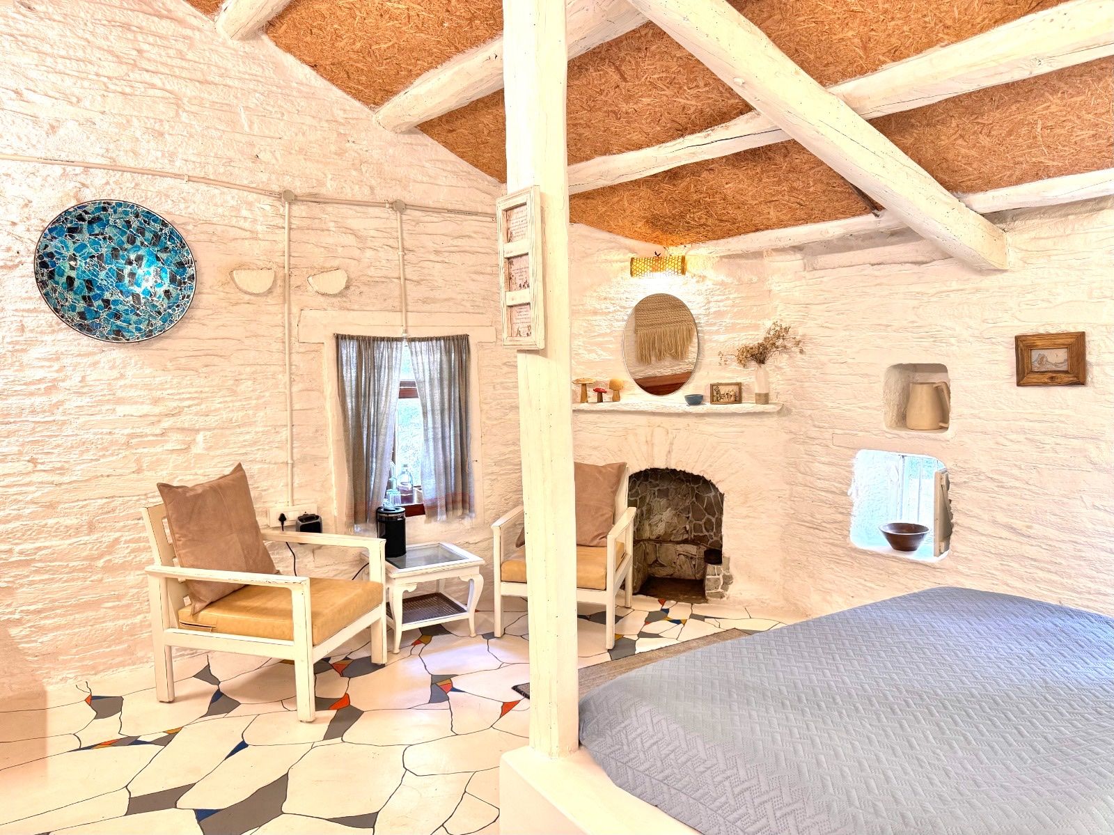 Two white chairs, a mosaic plate on the wall and the corner of the bed