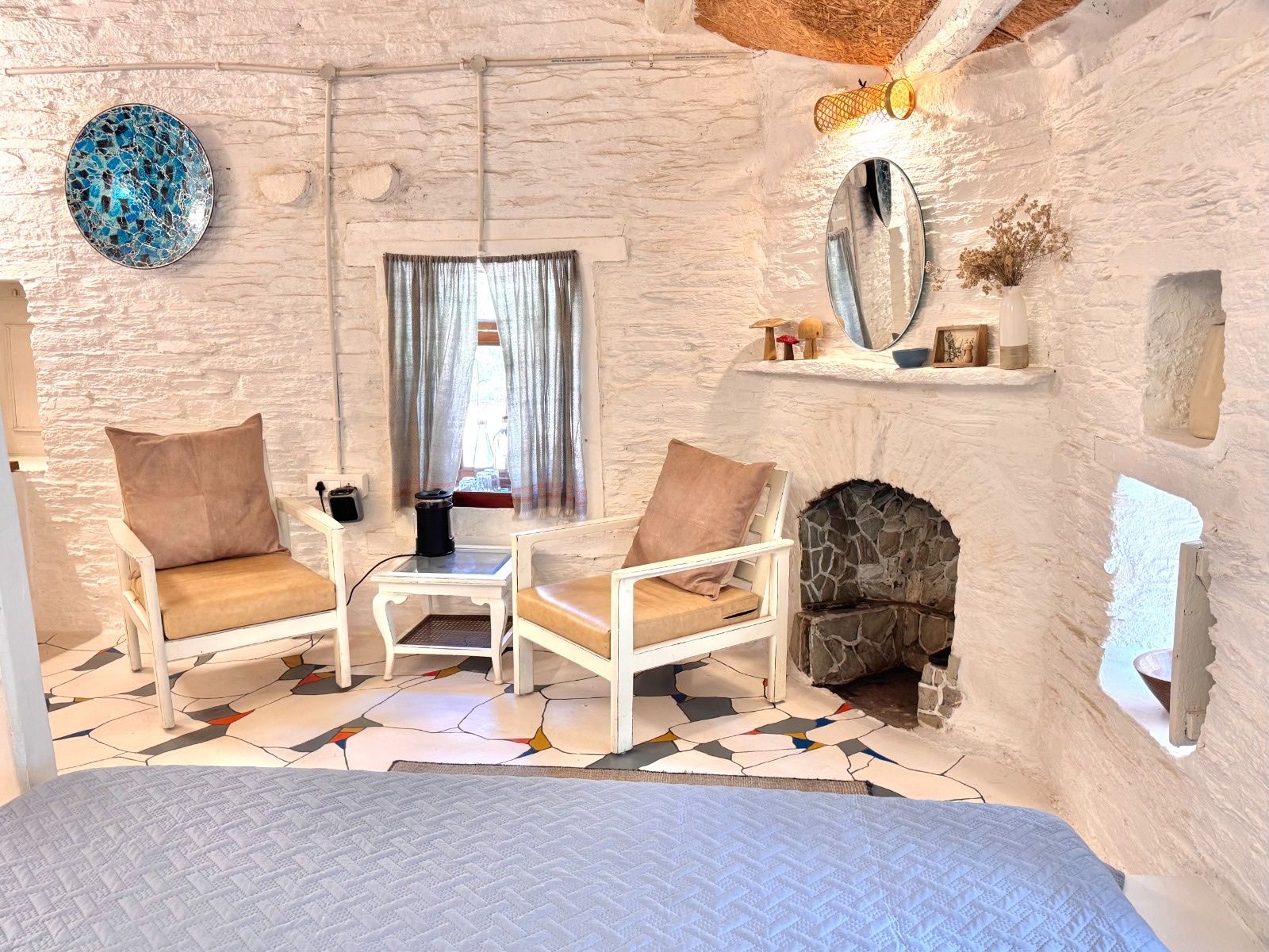 Two white chairs by a stone fireplace, with a blue mosaic plate on the wall