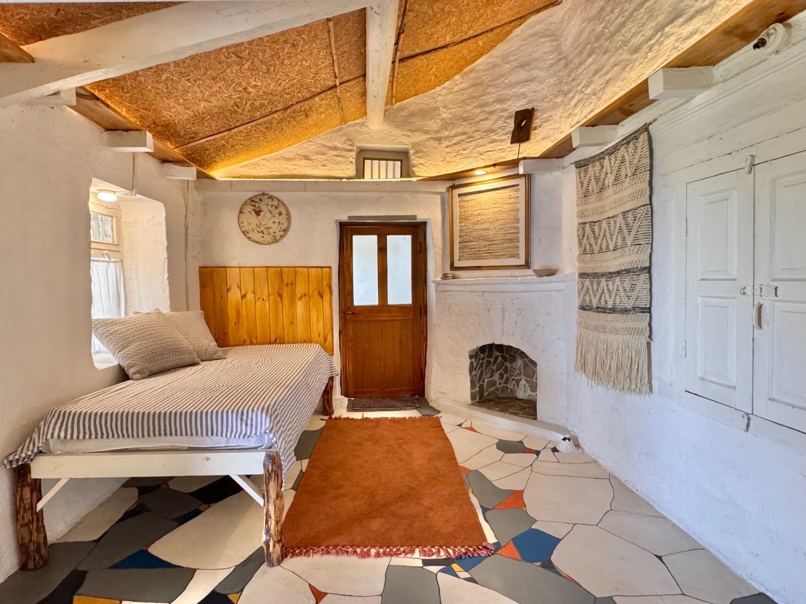 The study, with a day bed, an orange rug, a woven hanging and a small fireplace